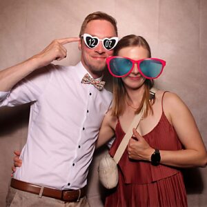 Zwei Personen in festlicher Kleidung vor einen Vintage Beigen Hintergrund mit witzigen Accessoires